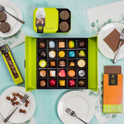 Overhead view of a 25 piece signature truffle box featuring the artistic quality of the chocolate. The contents of the gift bundle include: Hazelnut Chocolate Bar, S'mores Love, and Salted Caramel Pretzel Inclusion Bar. 